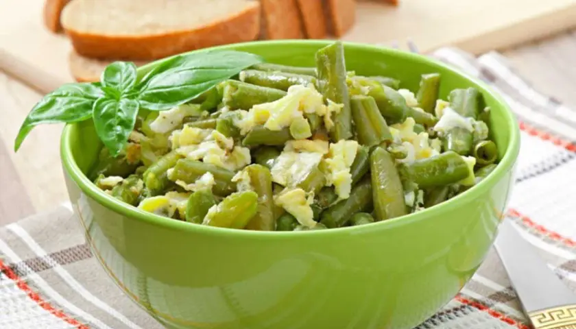 Salade haricots verts fraîchement préparée, garnie de basilic, servie dans un bol vert vif.