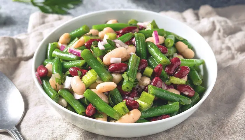 Salade colorée de haricots verts, haricots blancs et haricots rouges, avec des oignons rouges et du céleri. Un plat frais et savoureux.
