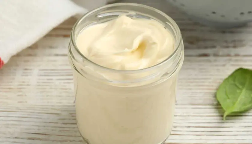 Un pot en verre rempli d'une onctueuse mayonnaise sans huile, sur une table en bois. Une feuille verte à côté.