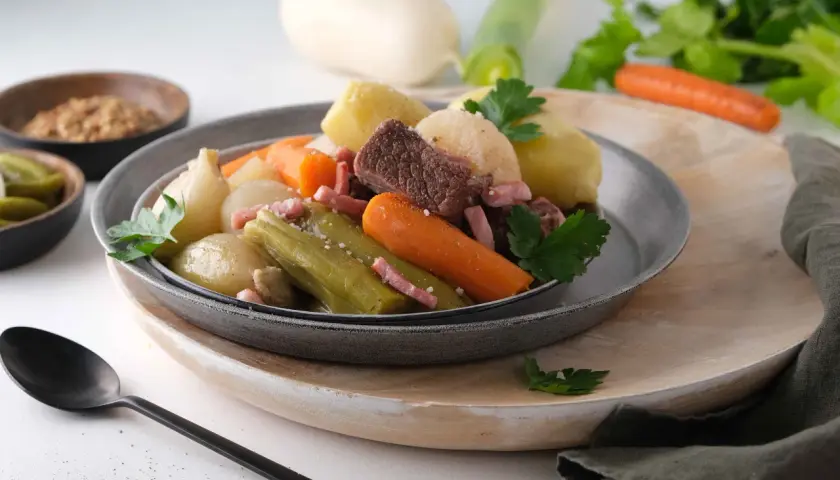 Pot-au-feu Cookeo avec viande, légumes (carottes, poireaux, oignons) et lardons, servi dans une assiette grise.