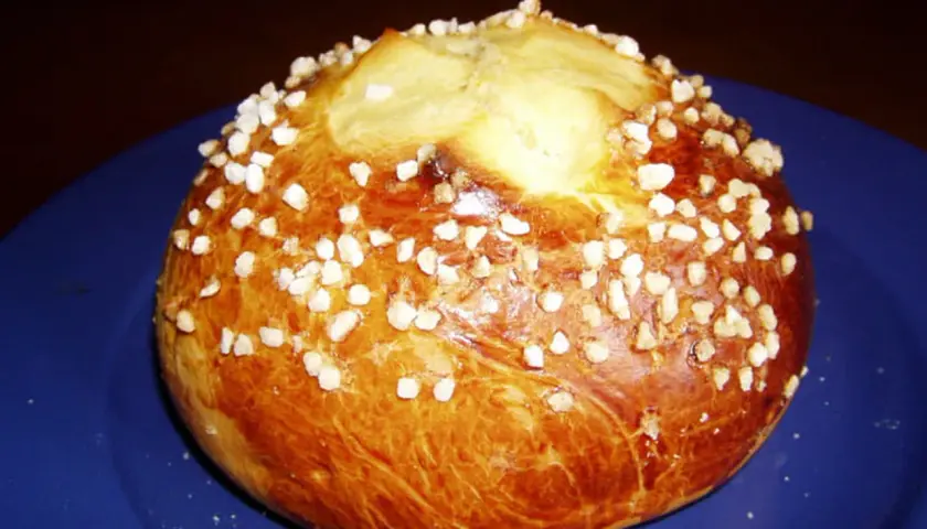 Mouna dorée parsemée de sucre perlé sur une assiette bleue.