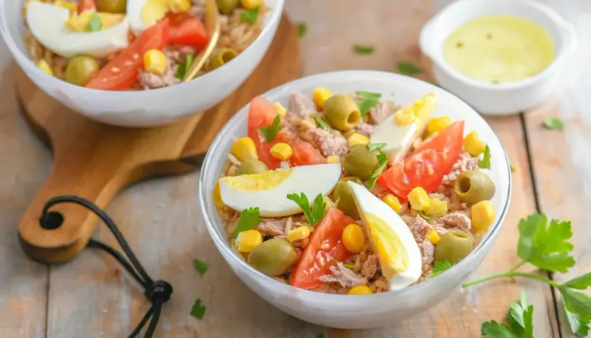 Salade niçoise au riz : thon, œufs durs, tomates, olives, maïs et persil frais. Un délice coloré.