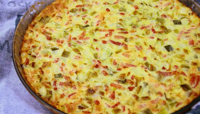 Une quiche aux légumes dorée et appétissante, garnie de poireaux et de lardons, sortant du four dans un plat en verre.