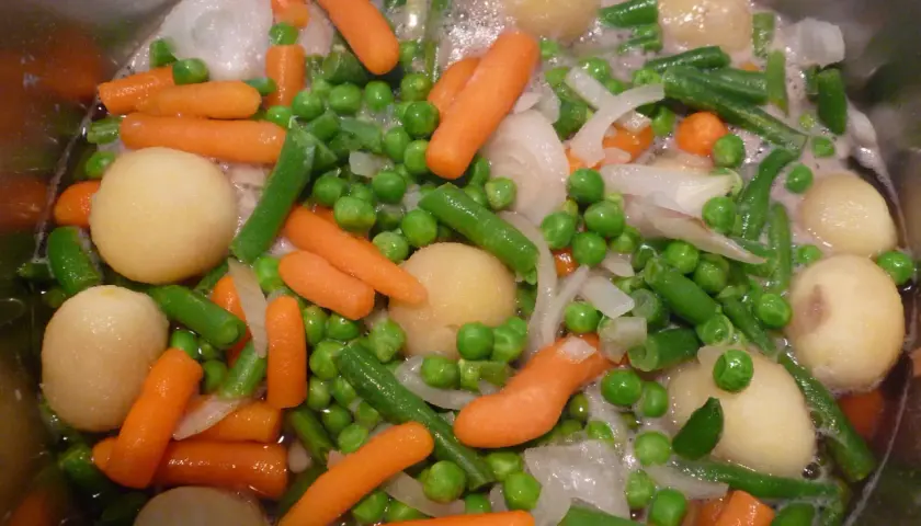 Gros plan sur une jardinière de légumes bouillant : carottes, petits pois, haricots verts, pommes de terre et oignons.