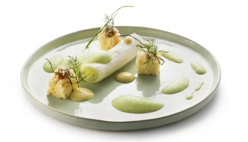 Poireaux à la crème, présentés avec des cubes de pain brioché, une sauce crémeuse et une mousse verte aérienne, le tout garni d'aneth.