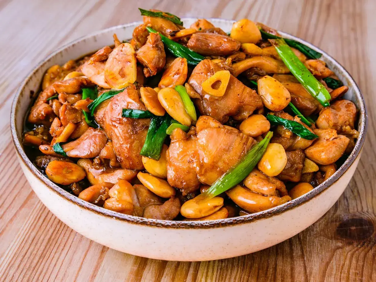 Un plat appétissant de poulet noix de cajou, garni d'oignons verts et d'ail, dans un bol sur une table en bois.