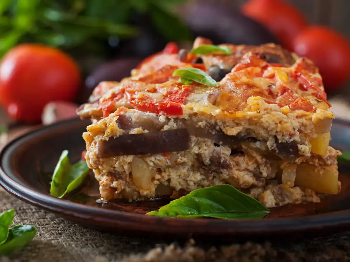 Un généreux flan de légumes, aux couches d'aubergines et de tomates, garni de basilic frais, sur une assiette en terre cuite.