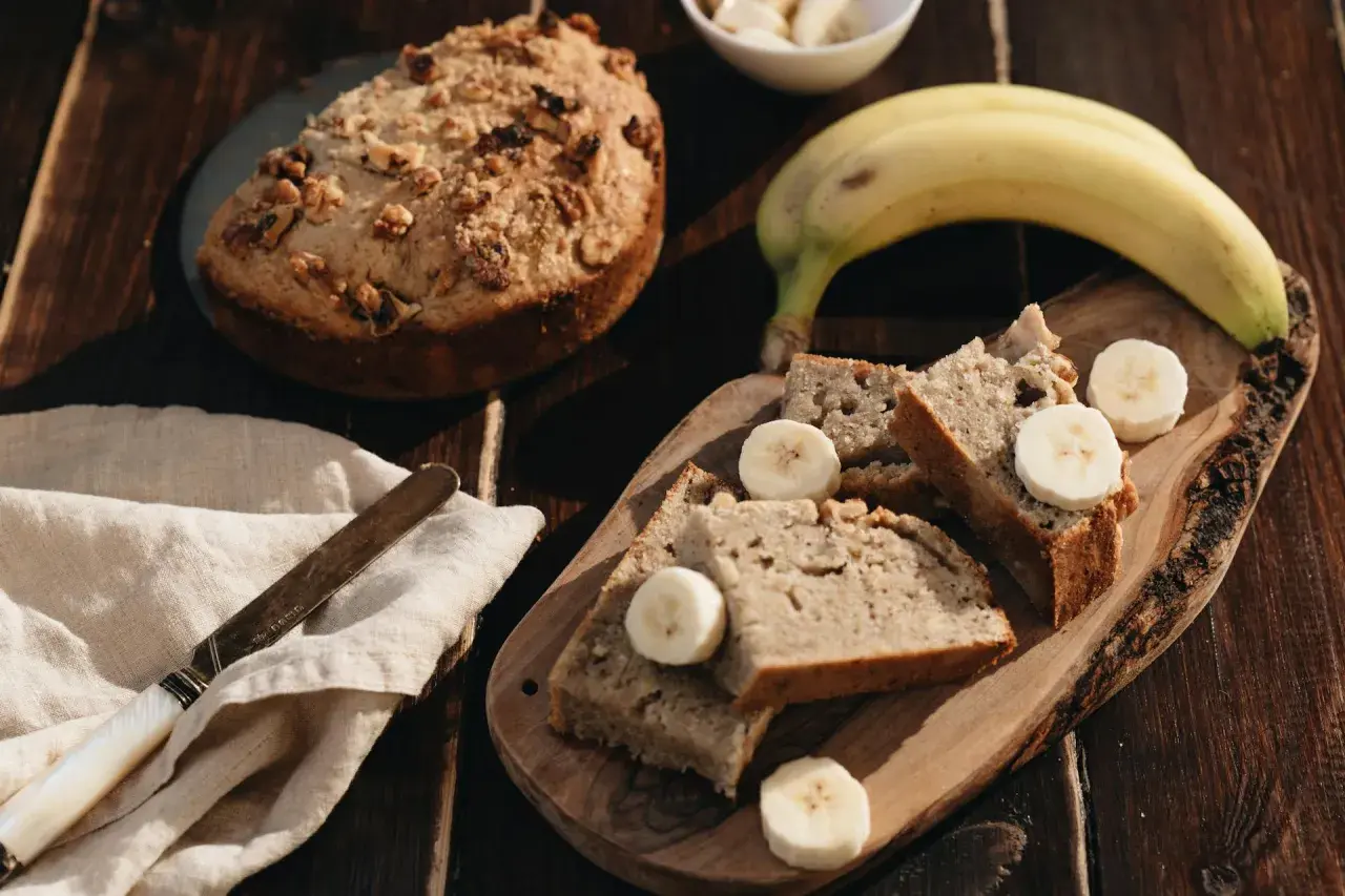 Tranches de banana bread moelleux, garnies de rondelles de banane fraîche, sur une planche en bois rustique. Un délice fait maison.