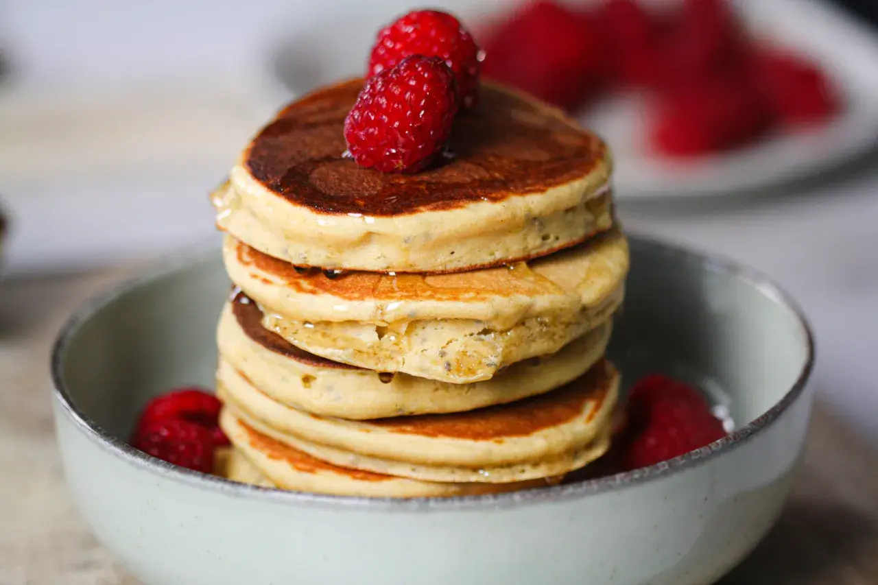 Pile de délicieux pancake sans gluten, garnis de framboises fraîches et nappés de sirop.