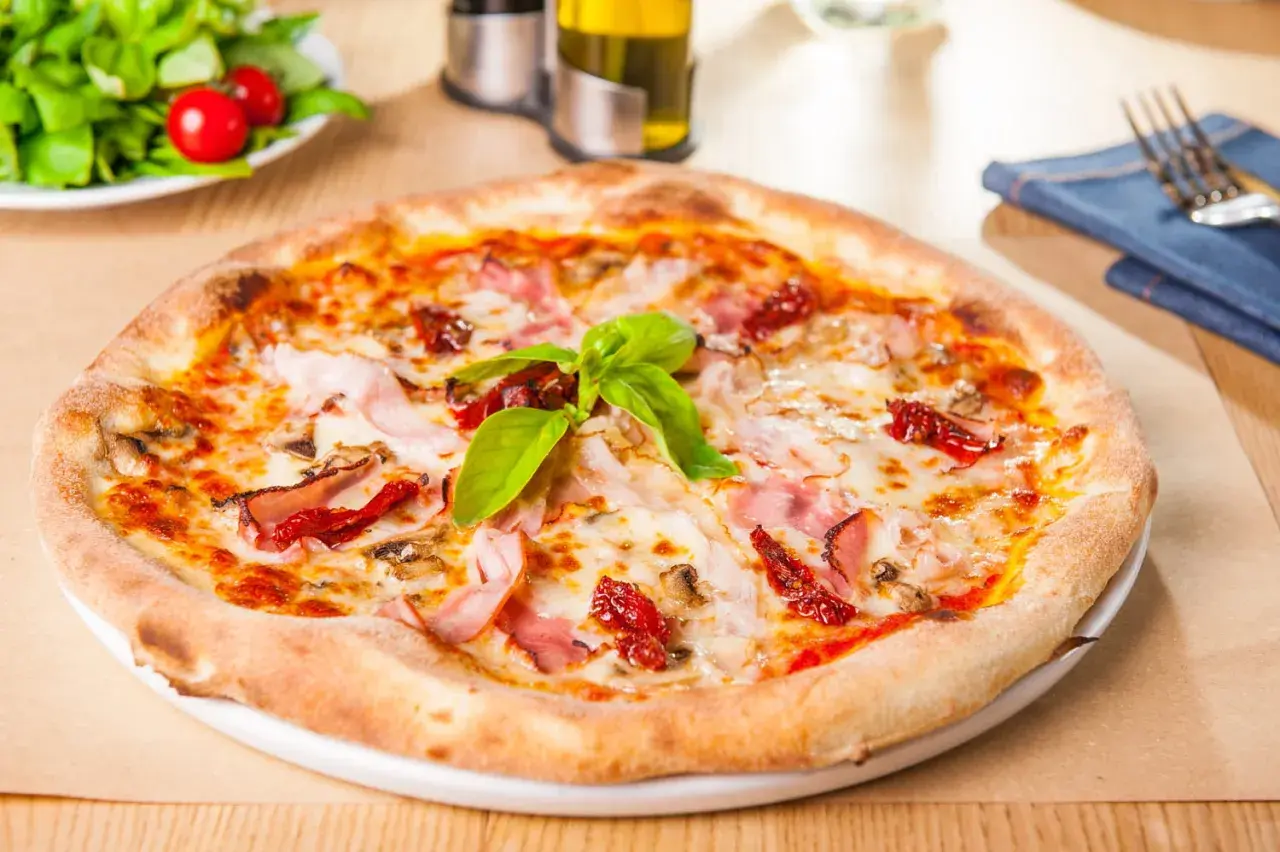 Une délicieuse pâte à pizza garnie de jambon, de tomates séchées et de basilic frais, prête à être dégustée.