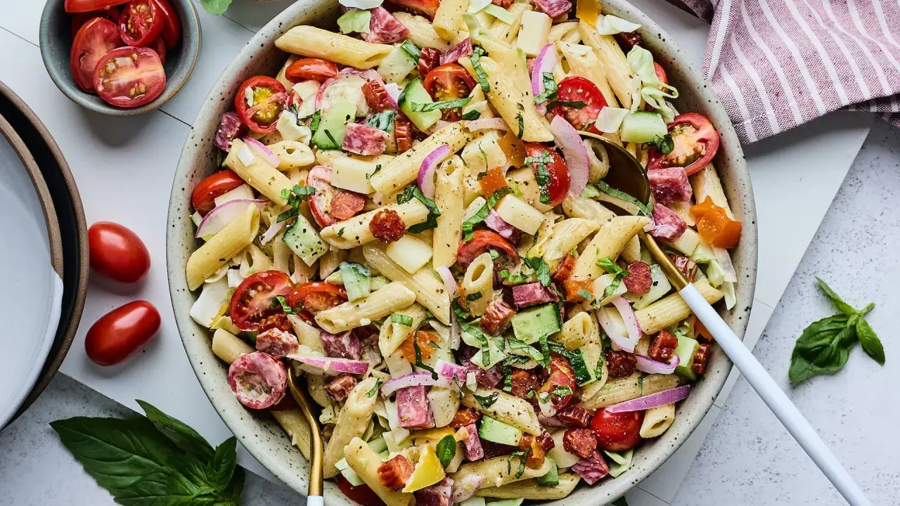 Salade de pâtes généreuse avec penne, tomates cerises, concombre, salami et oignons rouges. Un plat frais et coloré.