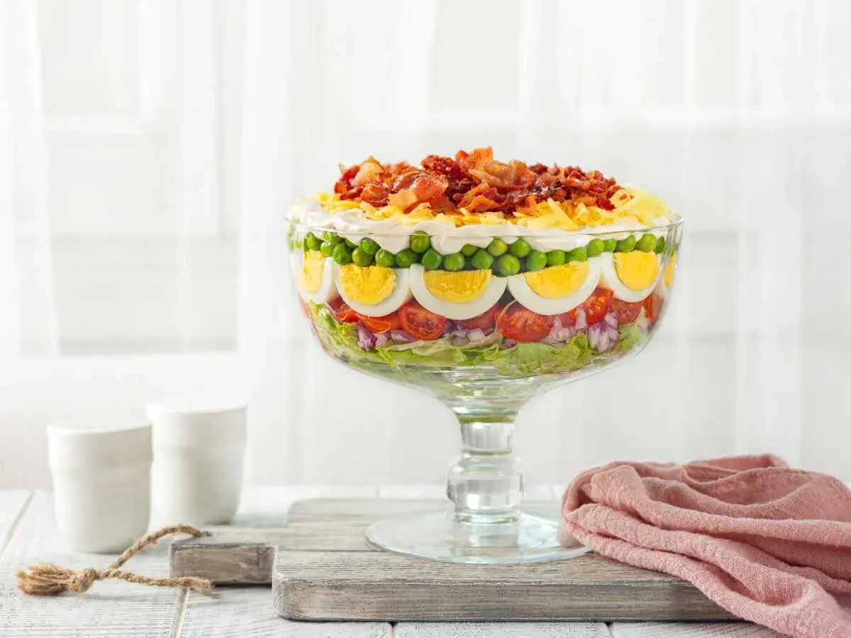 Une magnifique salade 7 étages, présentée dans un grand bol en verre, avec des couches de légumes frais, d'œufs durs, de petits pois et de bacon croustillant sur le dessus.