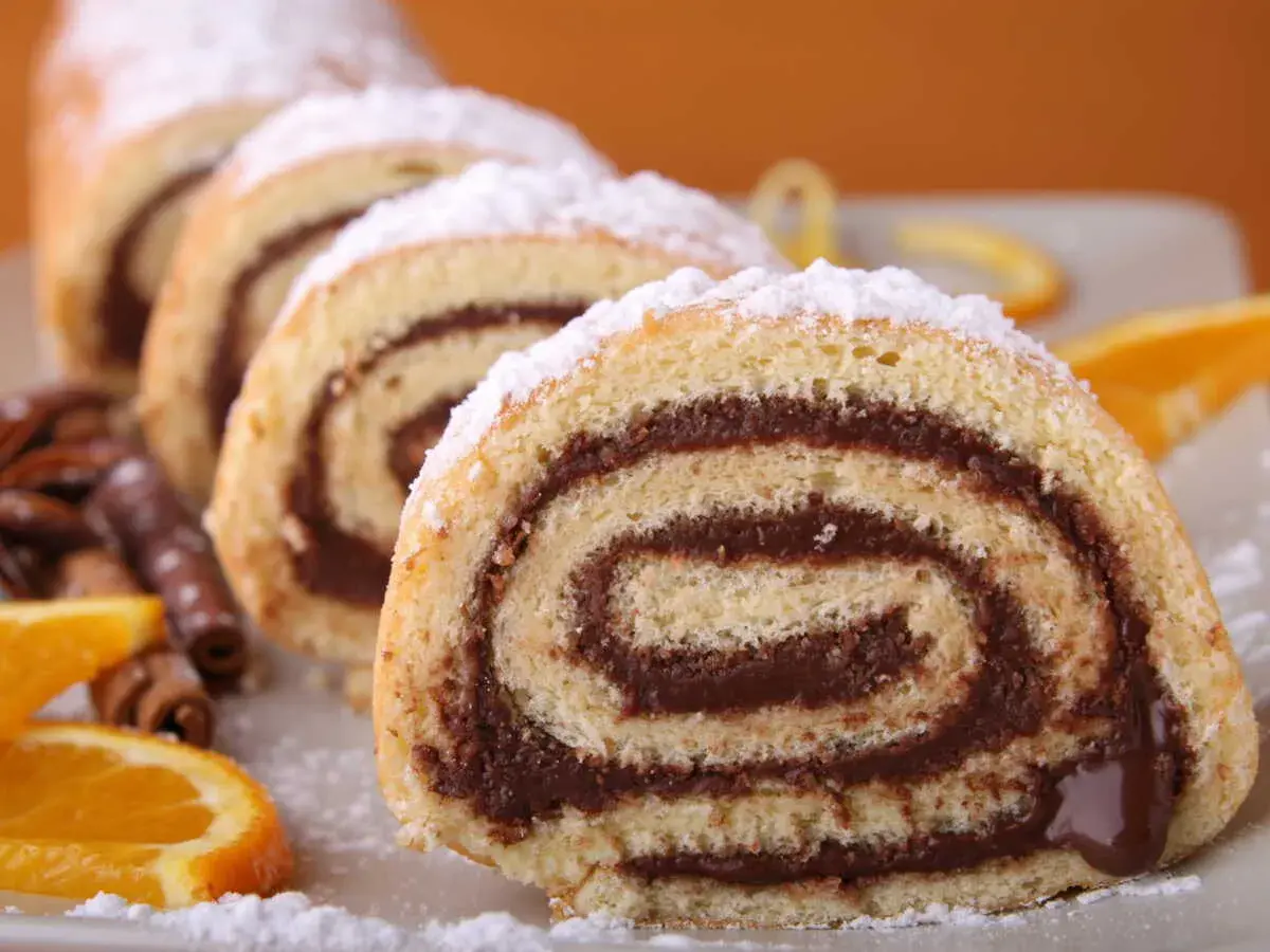 Tranches de roulé au chocolat saupoudrées de sucre glace, accompagnées d'oranges et de bâtons de cannelle.