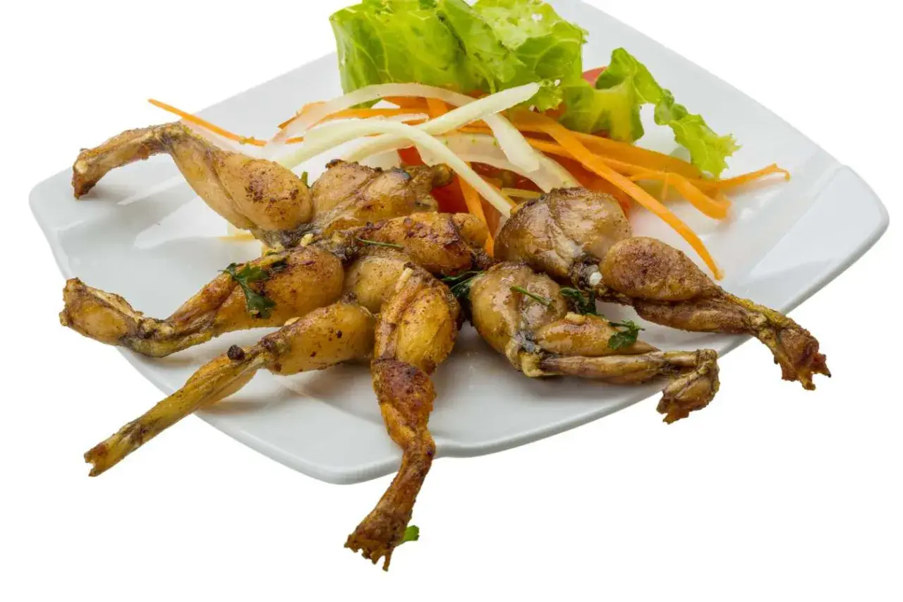 Assiette de cuisses de grenouille grillées, garnie de salade verte, d'oignons et de carottes râpées.