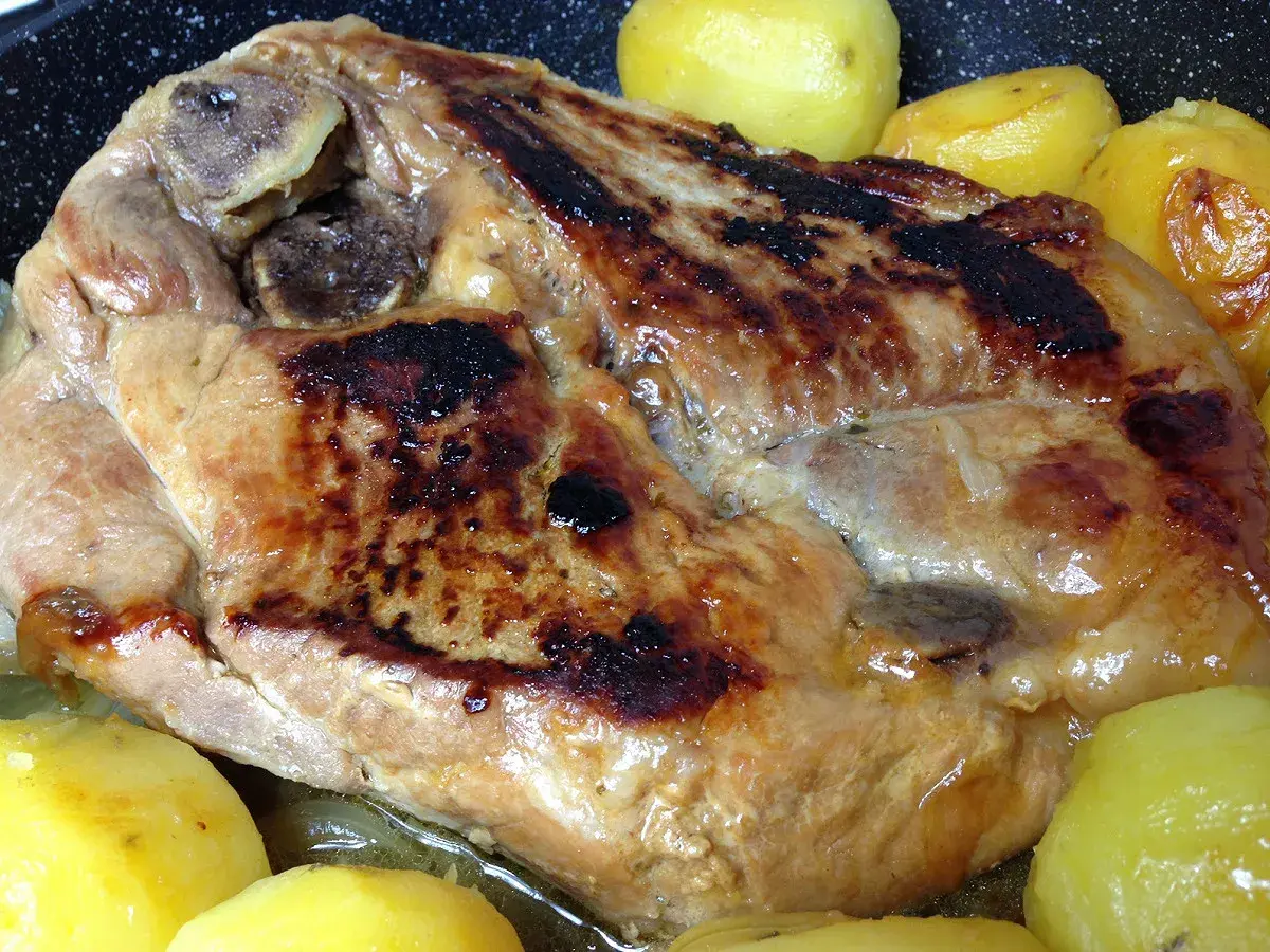 Rouelle de porc dorée et juteuse, accompagnée de pommes de terre fondantes, prête à être dégustée.
