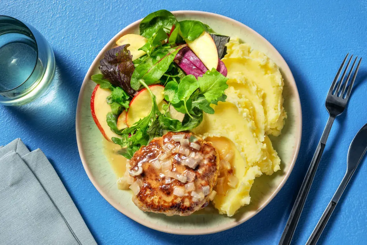 Un steak haché sauce oignons, servi avec une généreuse portion de purée de pomme de terre et une salade croquante aux pommes.