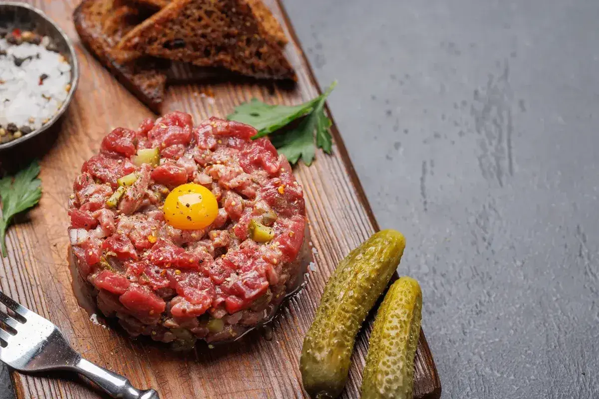 Un délicieux tartare de boeuf, garni d'un jaune d'œuf, servi avec des cornichons, du pain grillé et des épices.