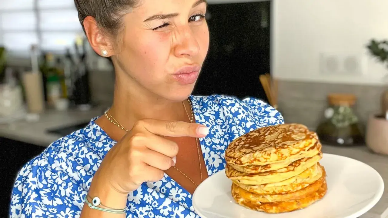 Une femme fait un clin d'œil et pointe du doigt une pile de pancakes banane sans oeuf sur une assiette.
