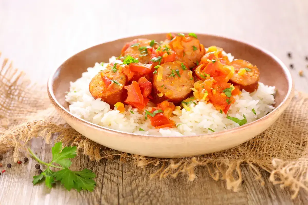 Un plat de rougail saucisse savoureux, avec des morceaux de saucisses épicées sur un lit de riz blanc, garni de persil frais.