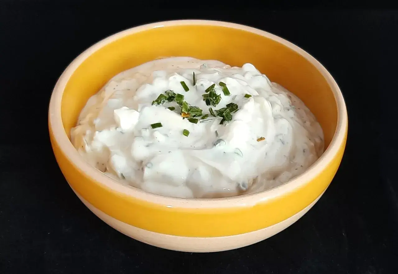 Sauce onctueuse à base de fromage blanc et de ciboulette fraîche, garnie de brins d'herbe verte.