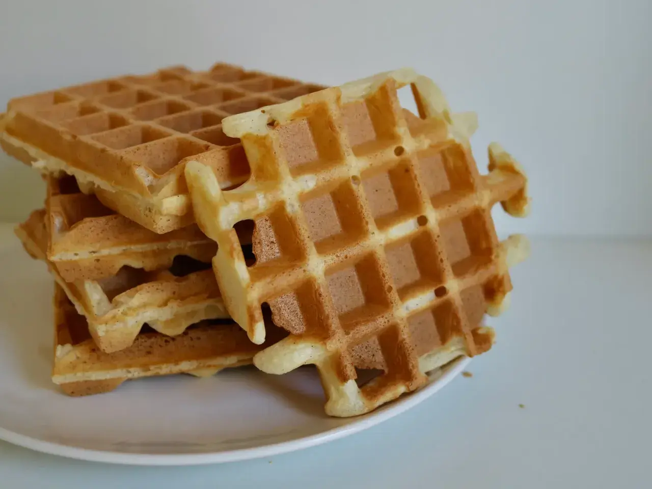 Pile de gaufres dorées sur une assiette blanche. La pâte à gaufre a été cuite à la perfection, offrant une texture croustillante et moelleuse.