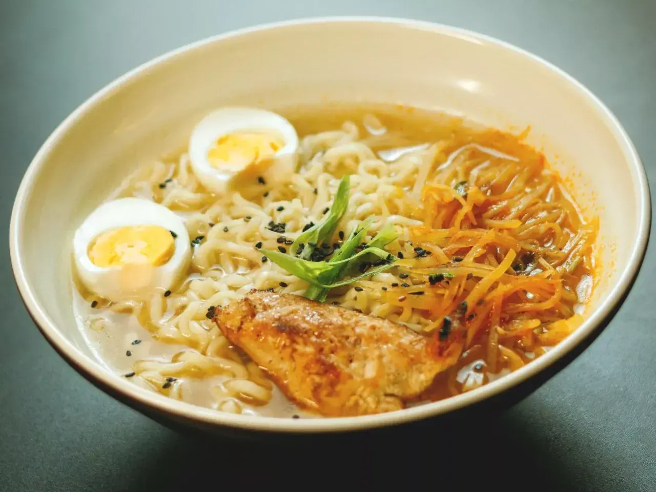 Un bol de recette ramen poulet, garni d'œufs durs, de poulet grillé, de nouilles et de ciboule.