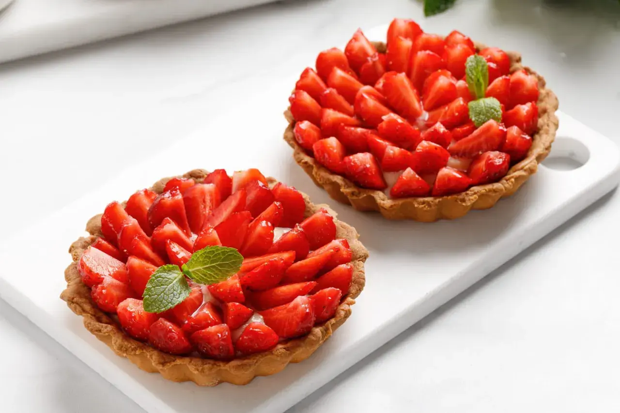 Deux tartelettes gourmandes aux fraises fraîches et crème pâtissière, ornées d'une feuille de menthe. Un délice estival.
