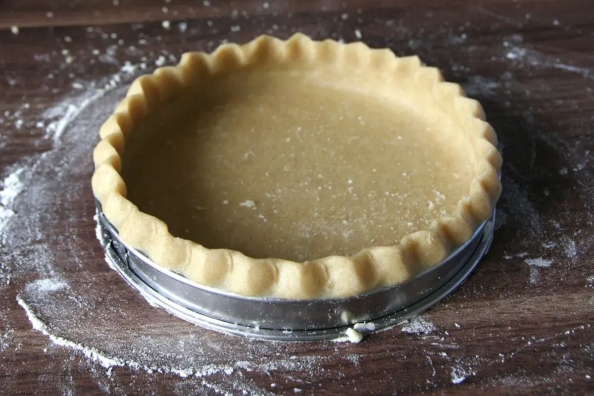Une pâte brisée maison, prête à être garnie, repose dans un moule à tarte sur une planche en bois.