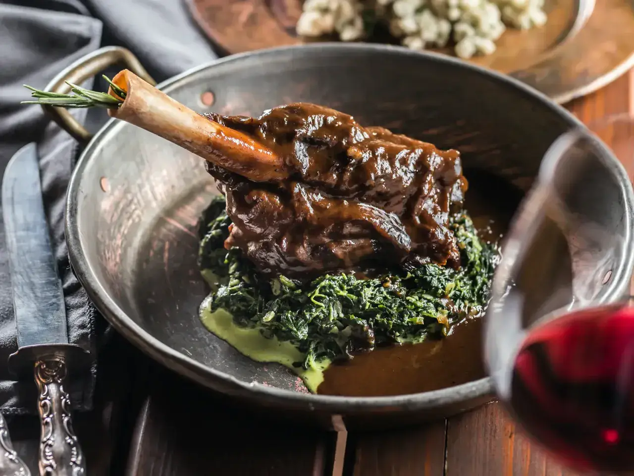 Un gigot de 7 heures, tendre et savoureux, servi sur un lit d'épinards crémeux dans un plat en cuivre. Une touche de romarin sur l'os promet un délice.
