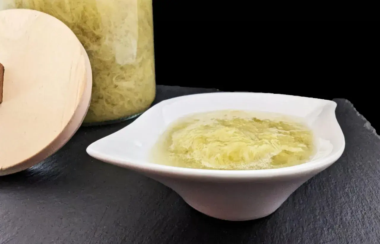 Compote de rhubarbe maison dans un bol blanc, à côté d'un bocal en verre rempli de cette délicieuse préparation.