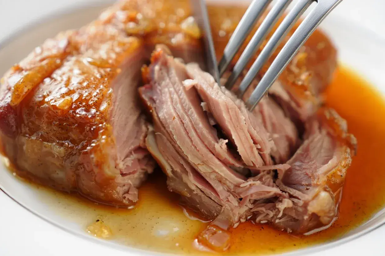 Une rouelle de porc juteuse, effilochée à la fourchette, baignant dans sa sauce dorée. Un délice pour une recette de rouelle de porc réussie.