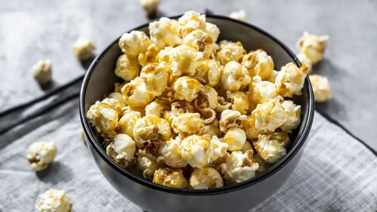 Un bol rempli de pop corn sucré, avec quelques grains éparpillés autour. Parfait pour une soirée cinéma !