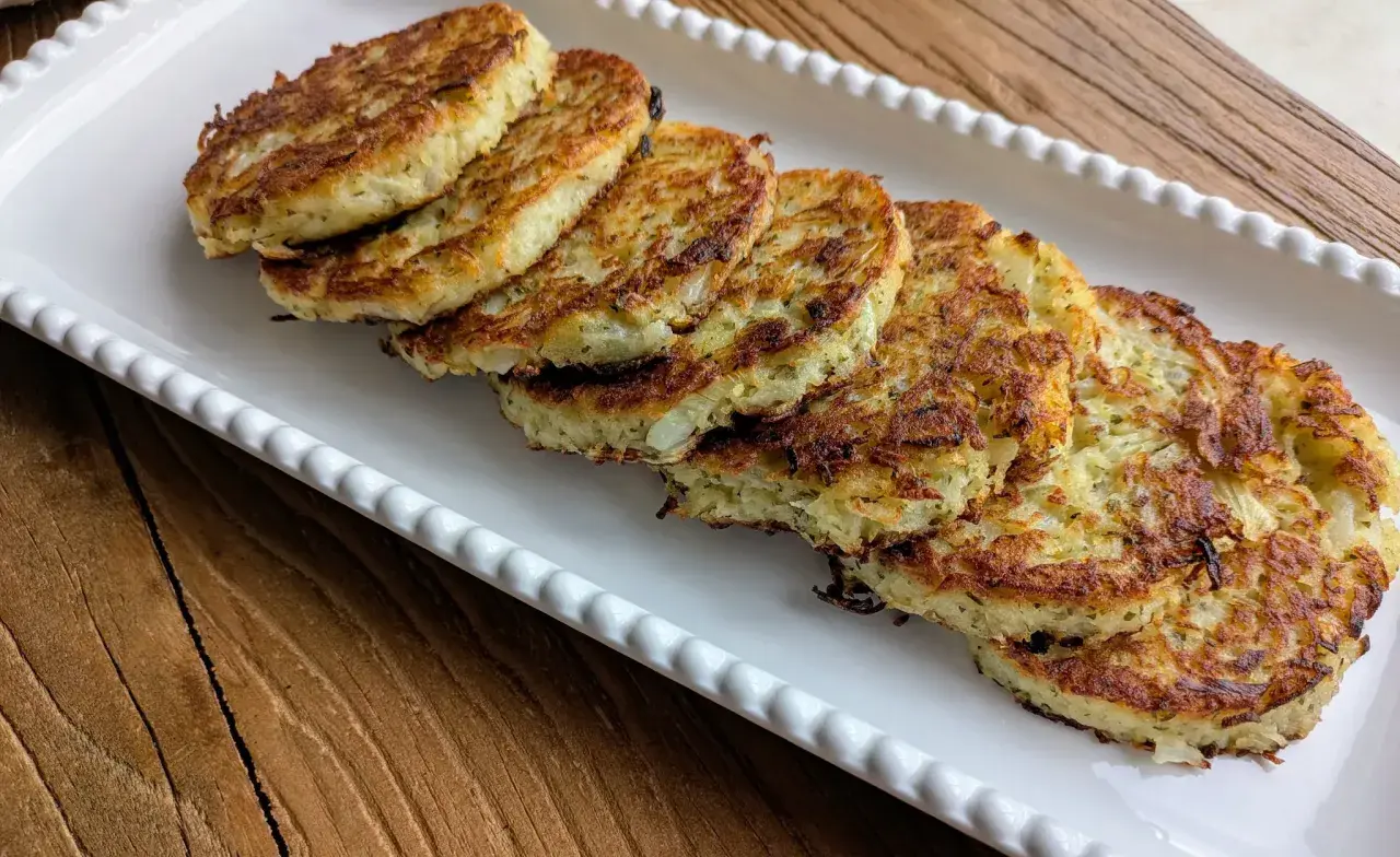 Six galettes de pomme de terre dorées et croustillantes, disposées sur un plat blanc festonné, prêtes à être dégustées.