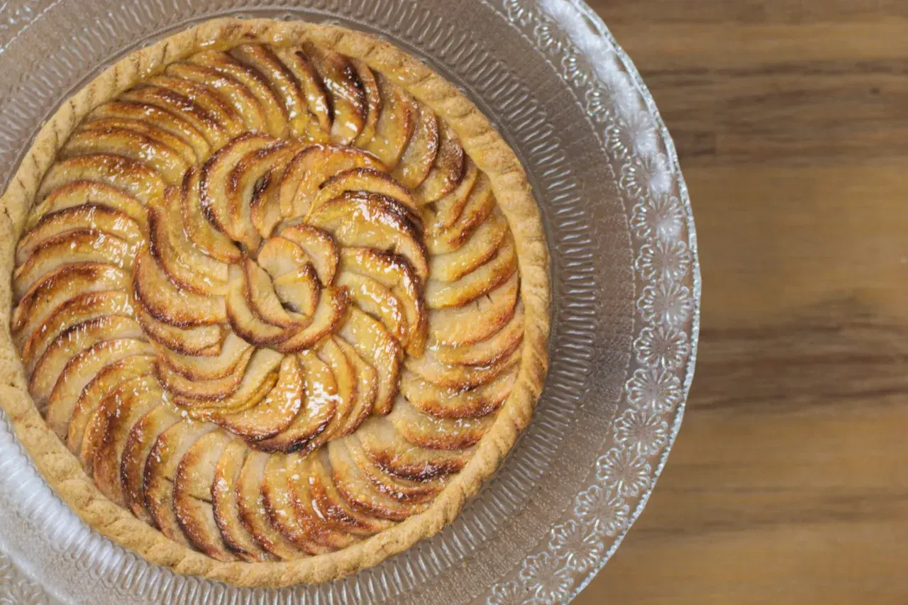 Tarte aux pommes magnifiquement arrangée en spirale sur un plat en verre, prête à être dégustée.