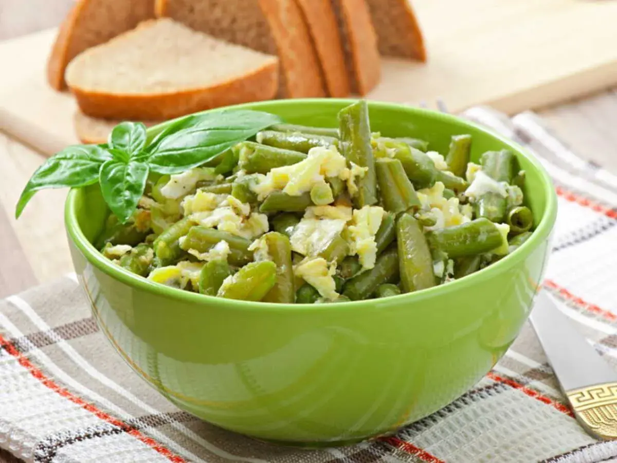 Salade haricots verts fraîchement préparée, garnie de basilic, servie dans un bol vert vif.
