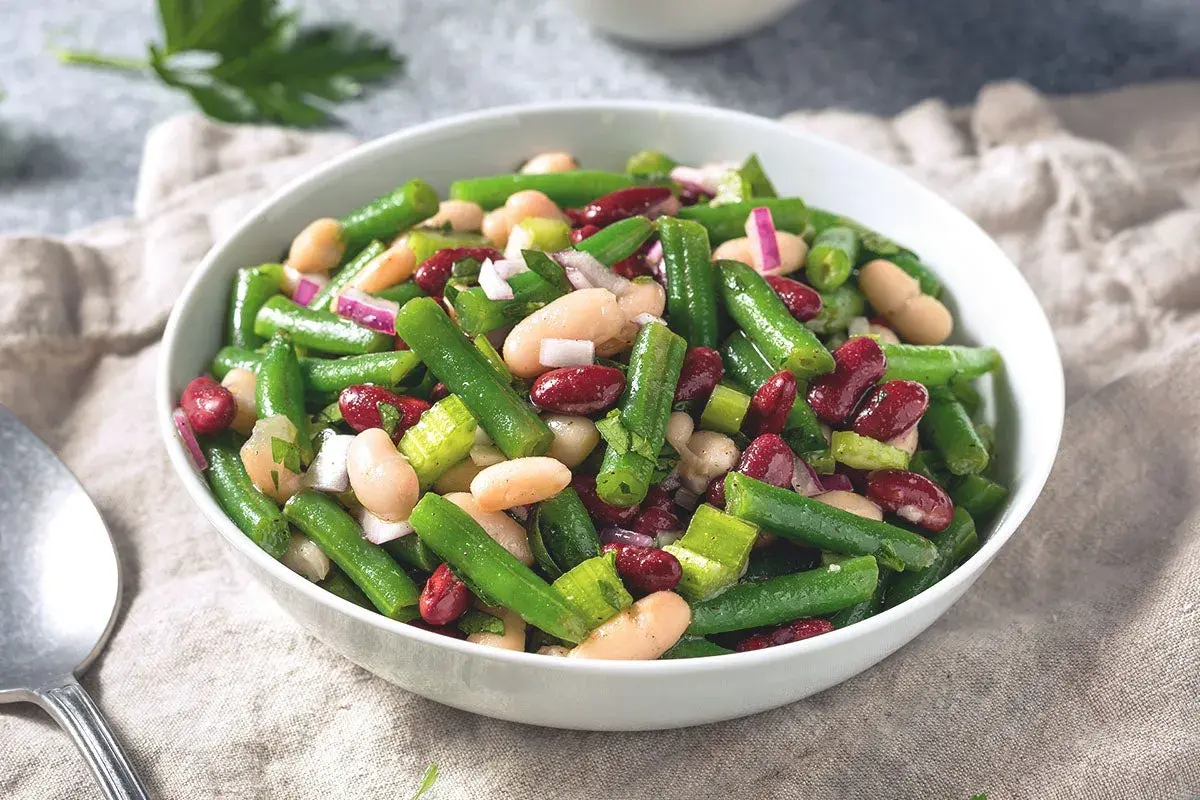 Salade colorée de haricots verts, haricots blancs et haricots rouges, avec des oignons rouges et du céleri. Un plat frais et savoureux.