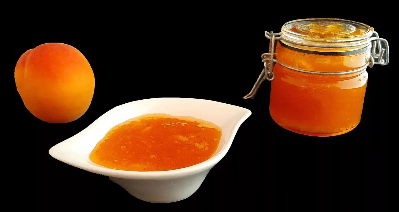 Un abricot frais à côté d'une coupelle de confiture abricot peu sucrée et d'un bocal de cette même confiture.
