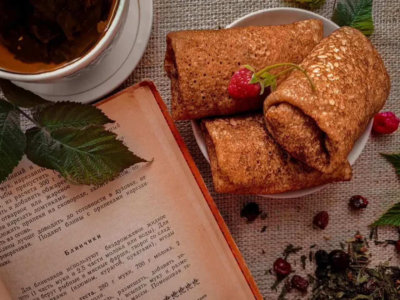 Crêpes roulées sur une assiette, accompagnées d'une tasse de thé et d'un livre de recette. Une framboise décore les crêpes. Parfait pour une recette crêpe.