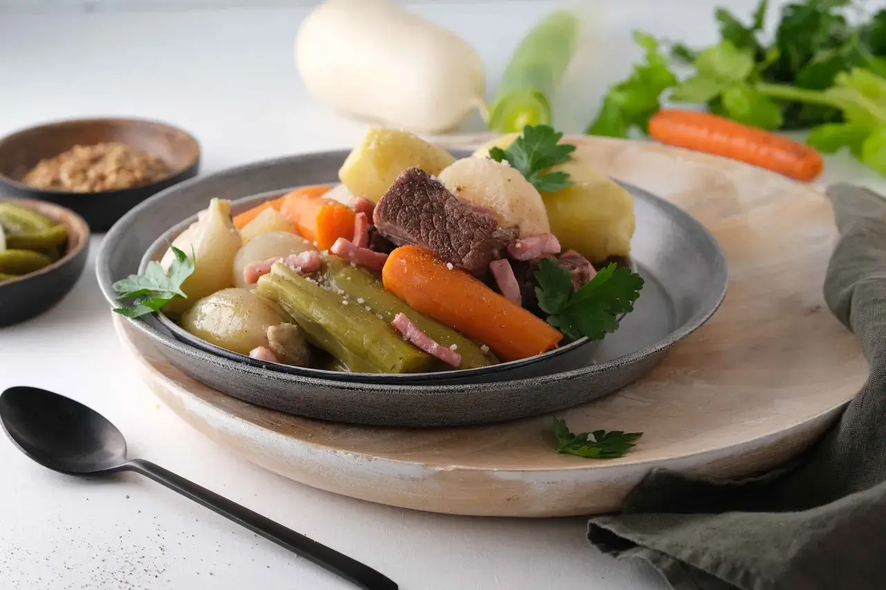Pot-au-feu Cookeo avec viande, légumes (carottes, poireaux, oignons) et lardons, servi dans une assiette grise.