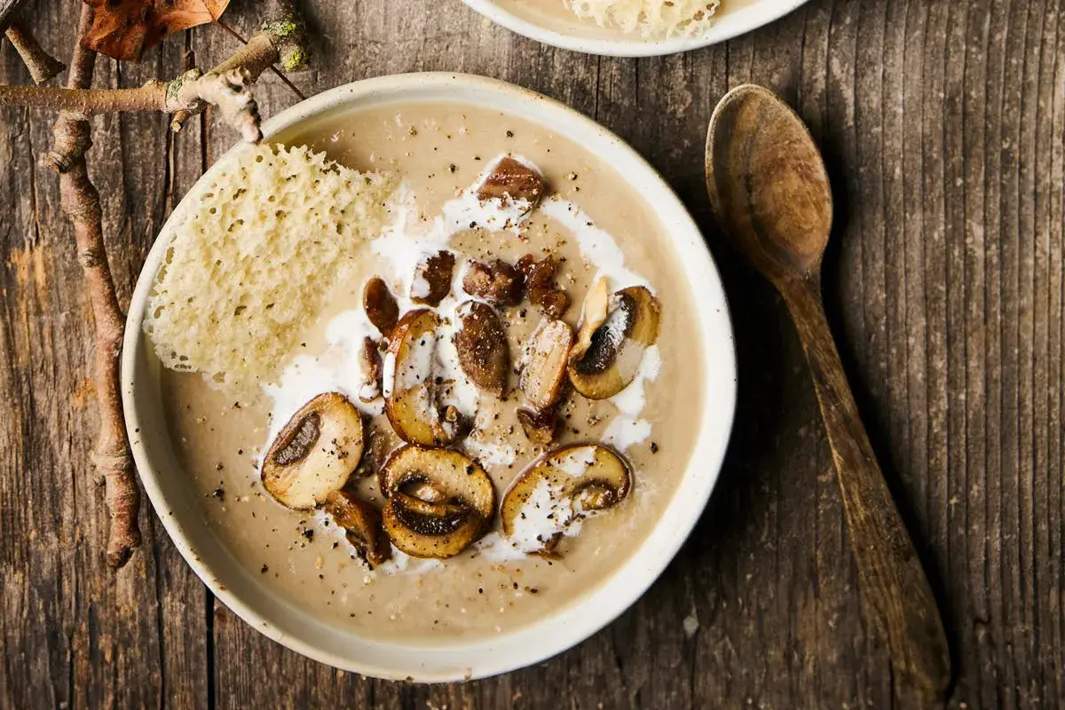 Un réconfortant velouté de champignons, garni de champignons sautés, de crème et d'une tuile de parmesan croustillante.