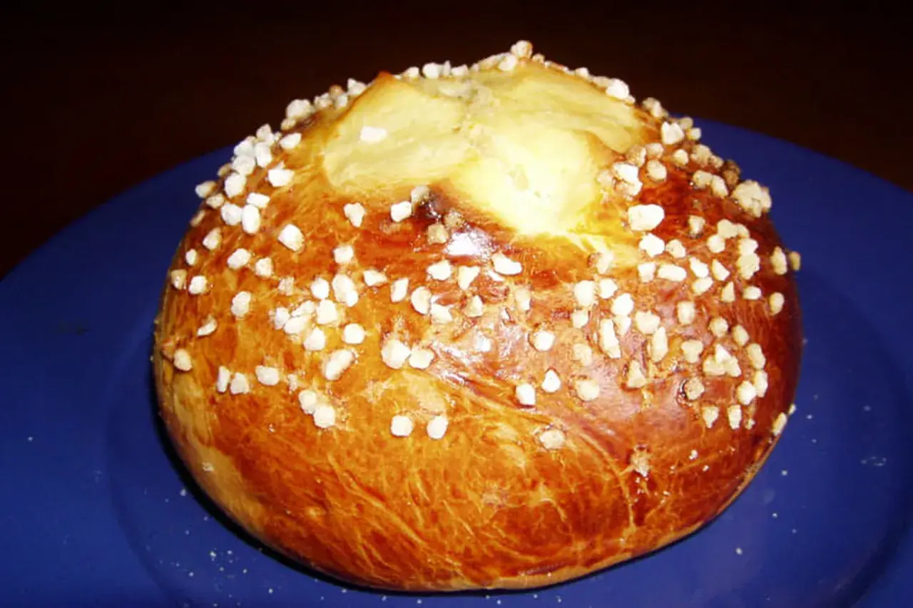 Mouna dorée parsemée de sucre perlé sur une assiette bleue.