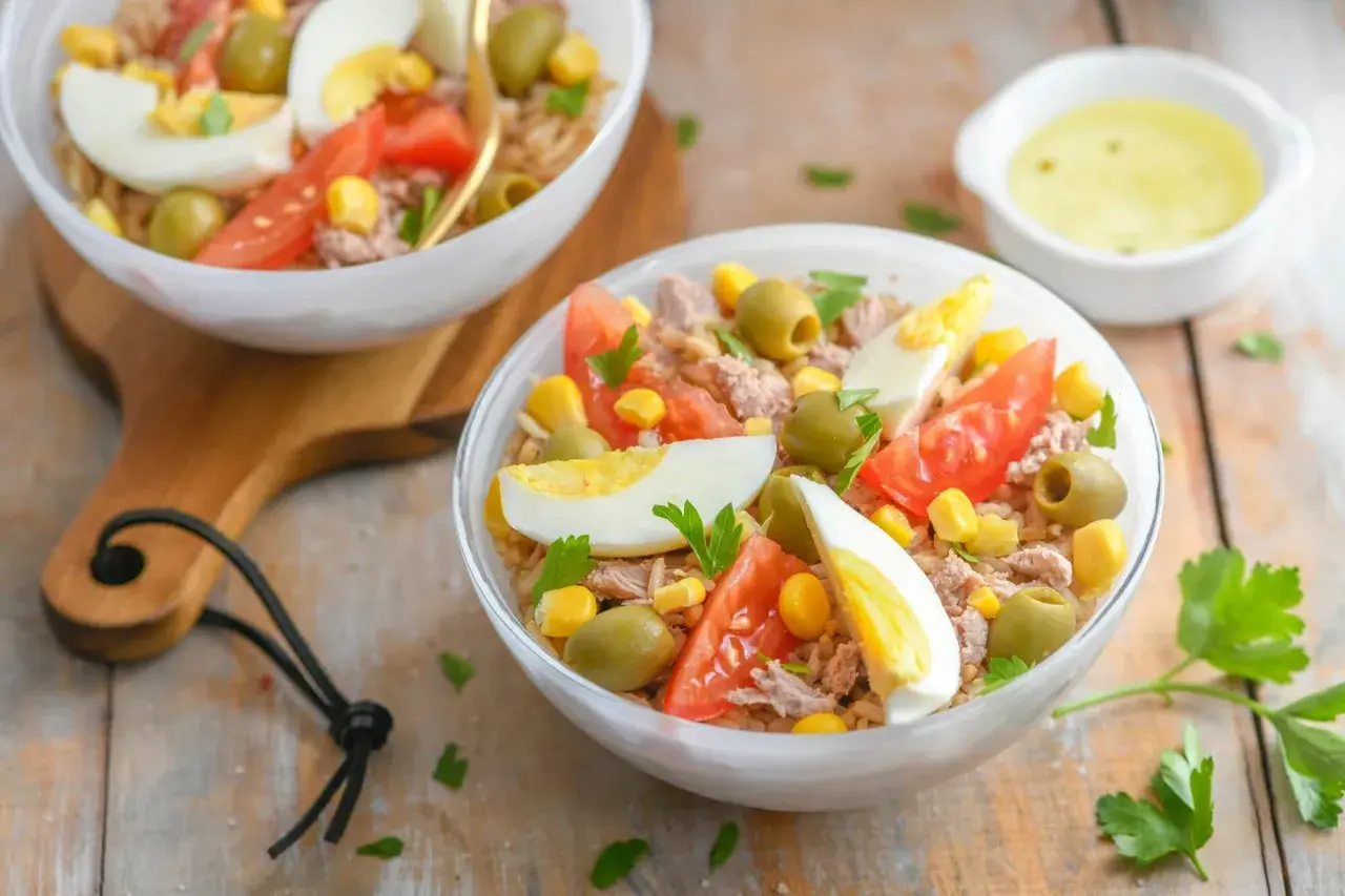 Salade niçoise au riz : thon, œufs durs, tomates, olives, maïs et persil frais. Un délice coloré.