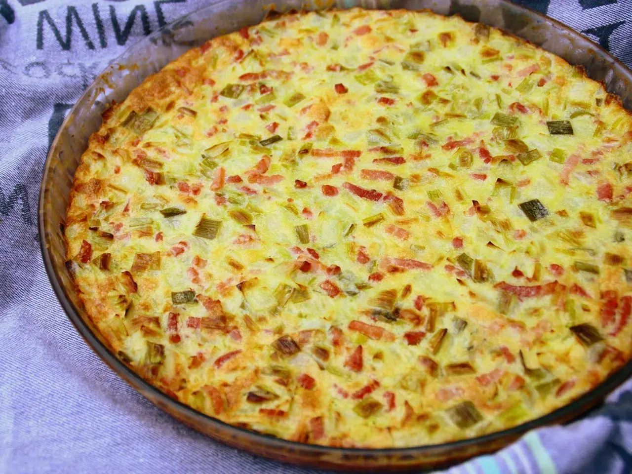 Une quiche aux légumes dorée et appétissante, garnie de poireaux et de lardons, sortant du four dans un plat en verre.