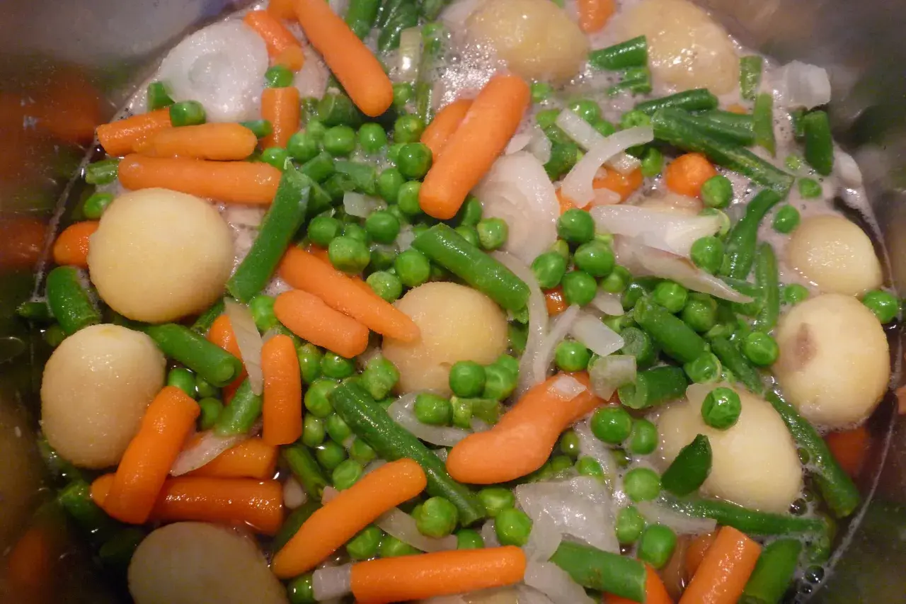 Gros plan sur une jardinière de légumes bouillant : carottes, petits pois, haricots verts, pommes de terre et oignons.