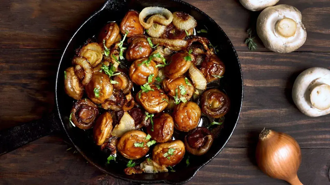 Champignons de Paris sautés à l'ail et aux oignons dans une poêle en fonte, parfaits pour une recette simple et savoureuse.