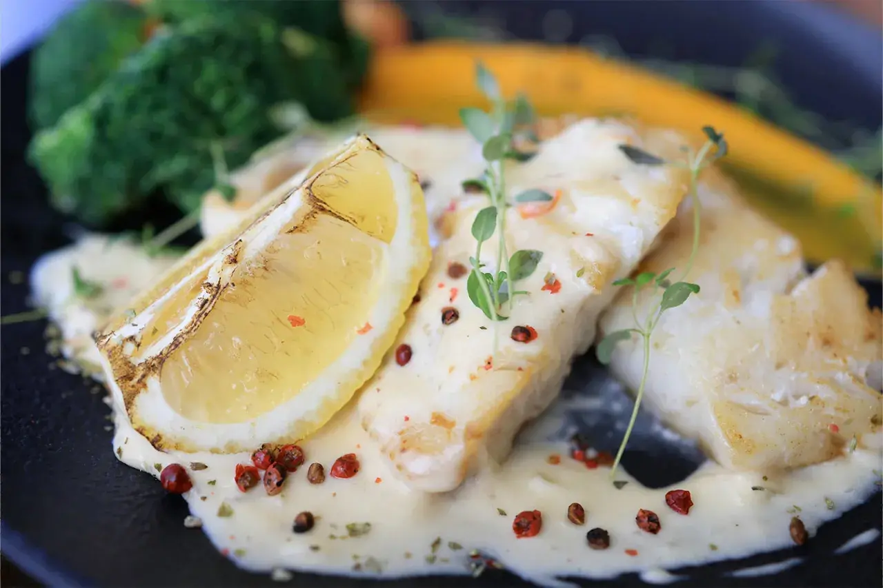 Filets de poisson nappés d'une sauce onctueuse, accompagnés d'une tranche de citron grillée et de légumes verts. Une sauce pour poisson parfaite pour sublimer ce plat.