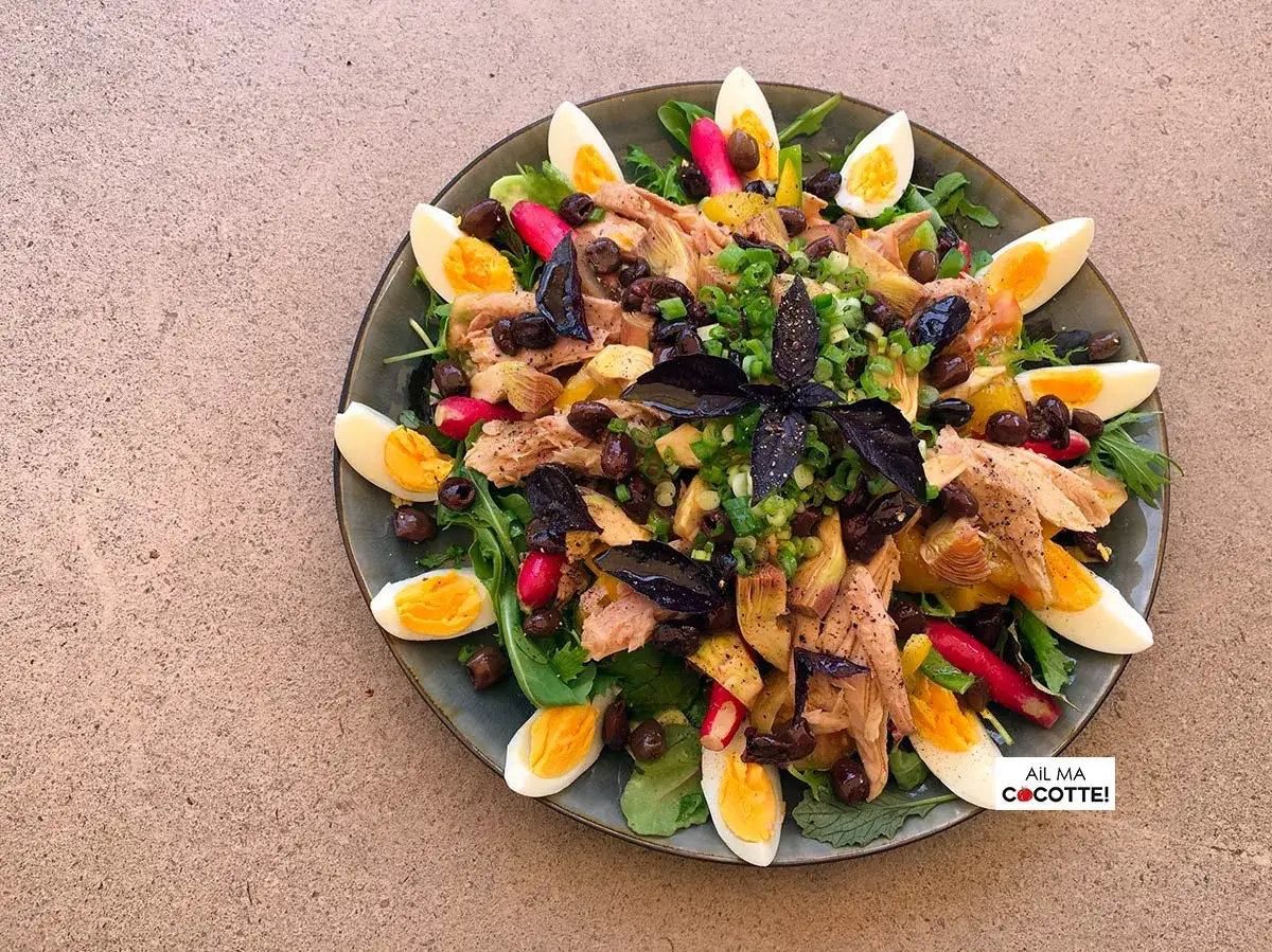 Salade niçoise avec riz, œufs durs, thon, olives, artichauts et radis, garnie d'herbes fraîches. Un délice coloré !