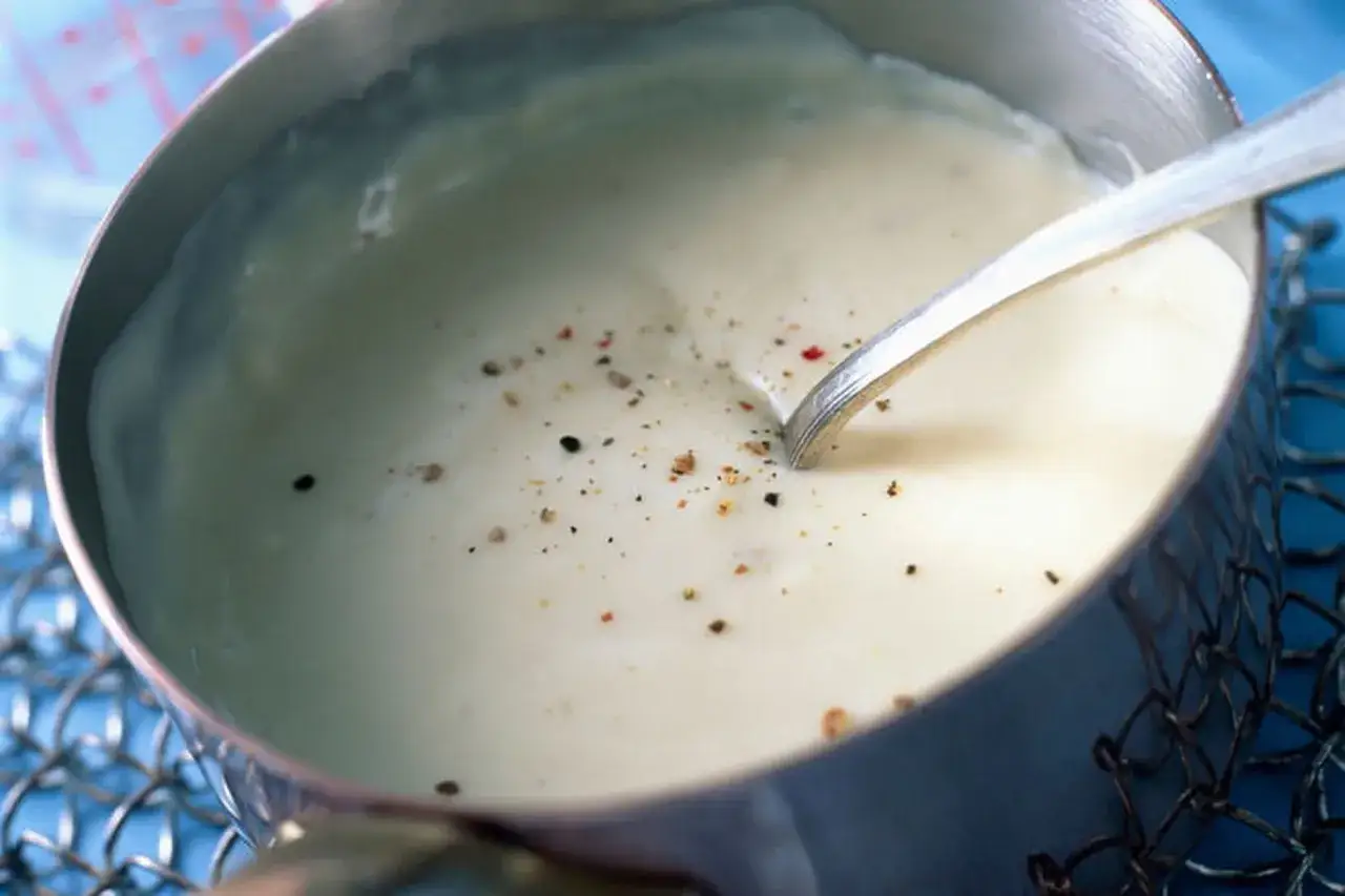 Sauce béchamel sans beurre, onctueuse et parsemée de poivre, prête à être utilisée dans une recette gourmande.