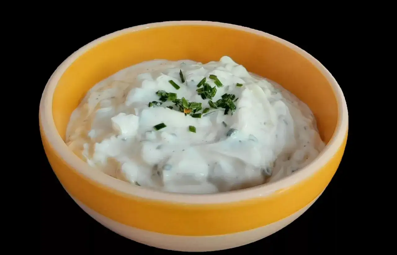Sauce onctueuse &agrave; base de fromage blanc et ciboulette fra&icirc;che, garnie de brins d'herbe verte, servie dans un bol jaune vif.