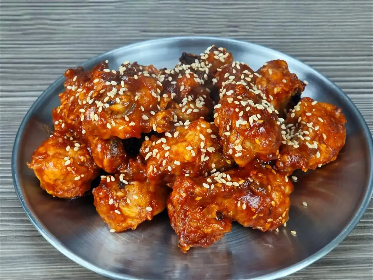 Un délicieux poulet air fryer croustillant, enrobé d'une sauce sucrée et salée, parsemé de graines de sésame.